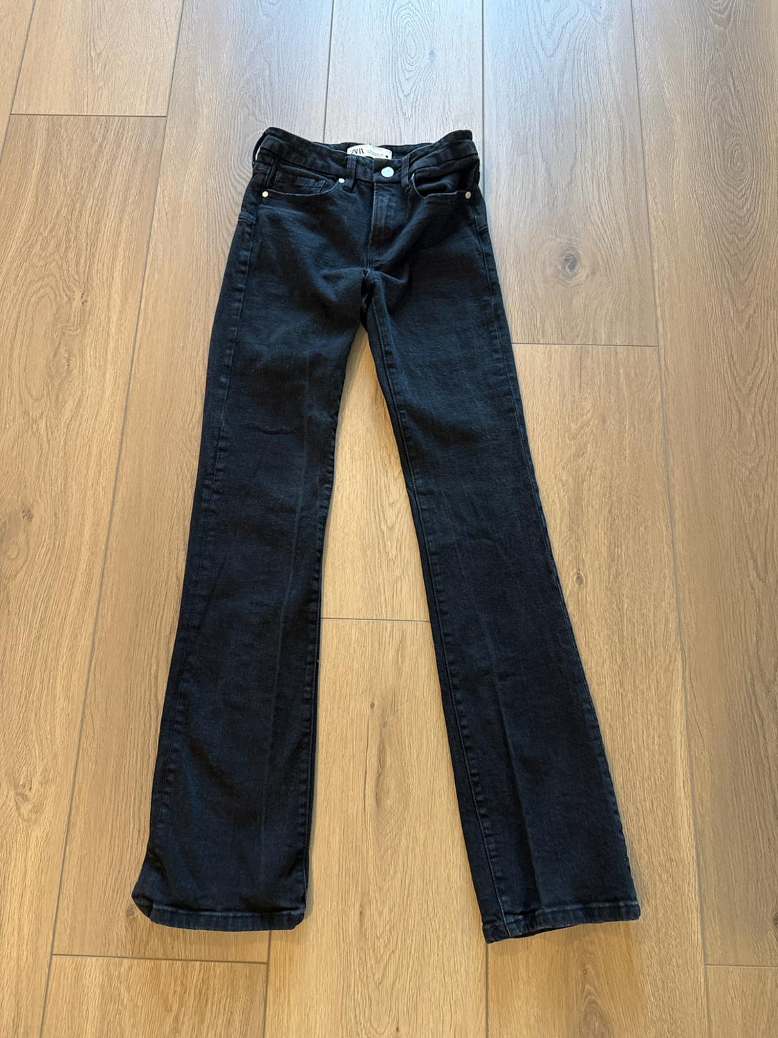 Black jeans spread out on a light wood floor.