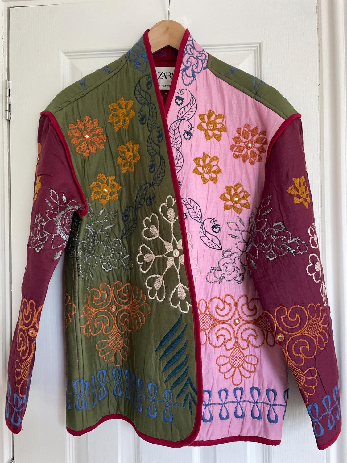 Jacket hung on a door, with an embroidered floral design in shades of green, pink, and burgundy. Visible label with text "ZARA".