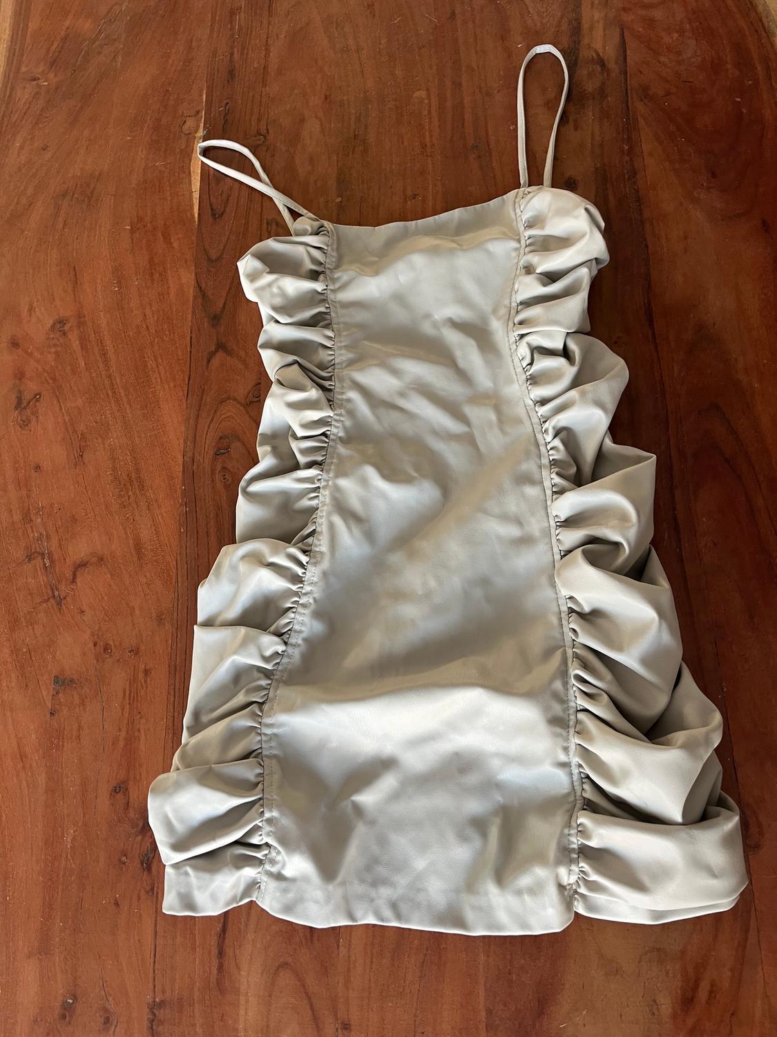 Beige dress with thin straps and side ruffles, on a brown wooden surface.