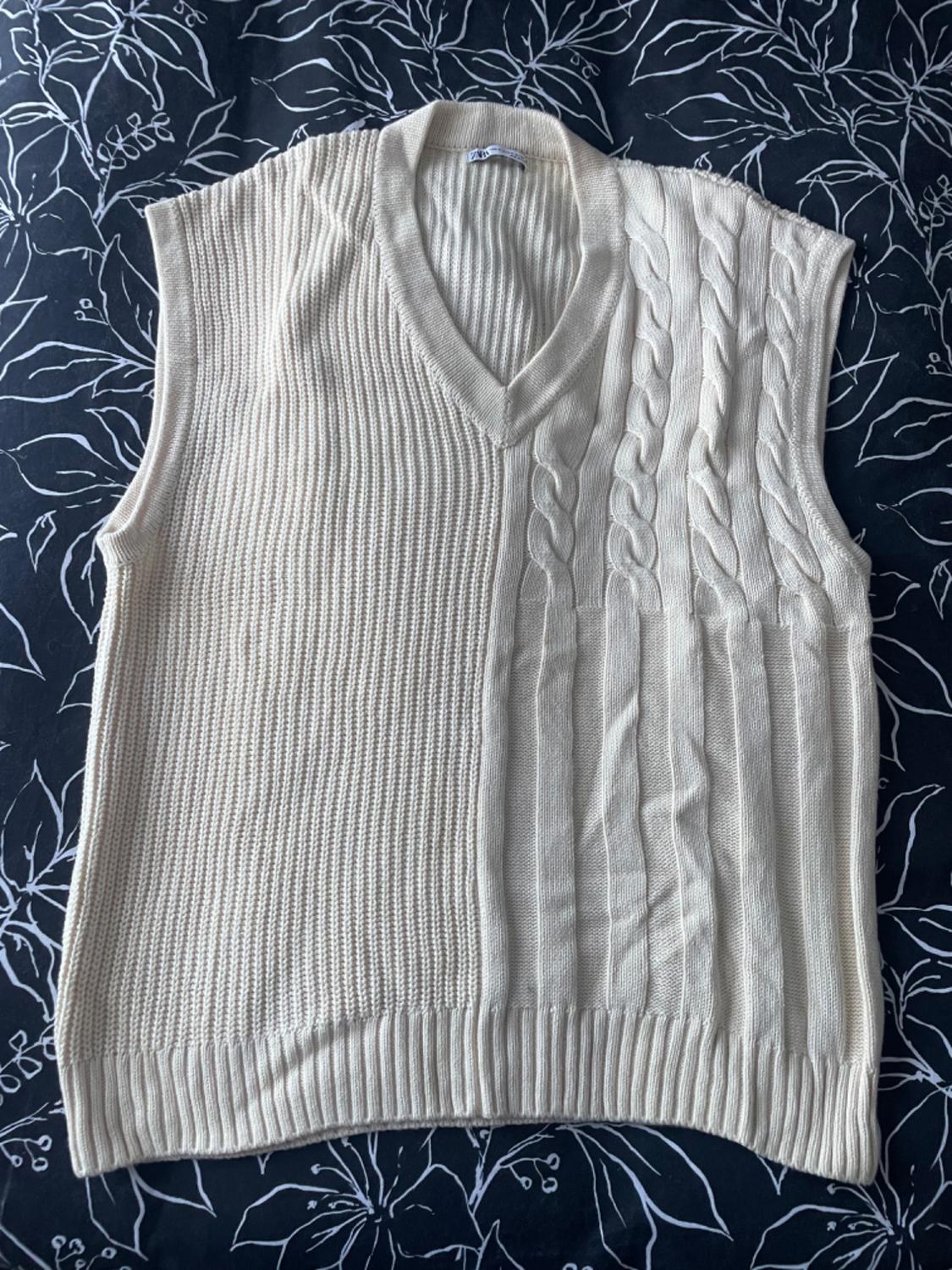 Beige knitted waistcoat with cable knit and vertical line design, on a black background with a white leaf pattern.