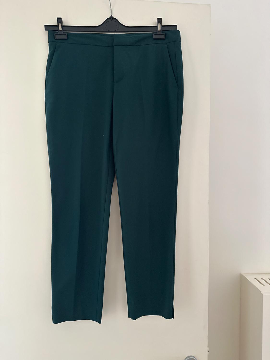 Dark green trousers hanging on a black hanger over a white door.