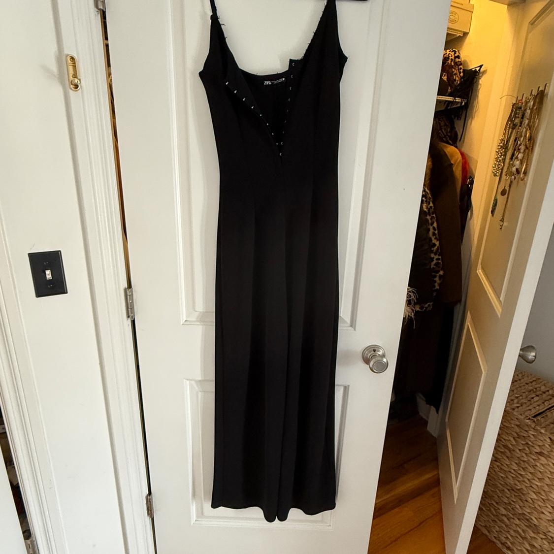 Long black dress with thin straps hanging on a white door. Wardrobe background with visible clothes and accessories.