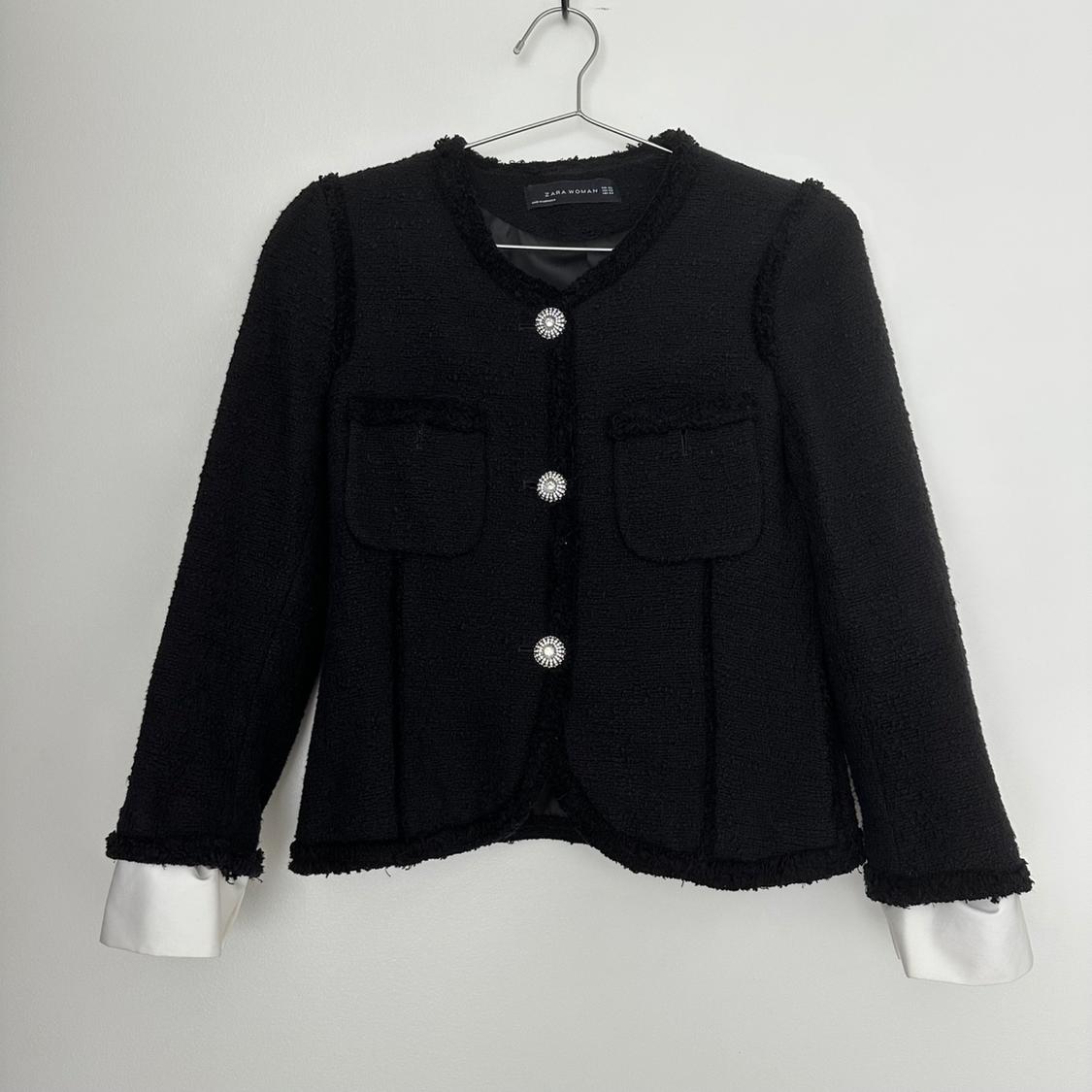 Black wool jacket with silver buttons and front pockets, hanging on a hanger against a white background.