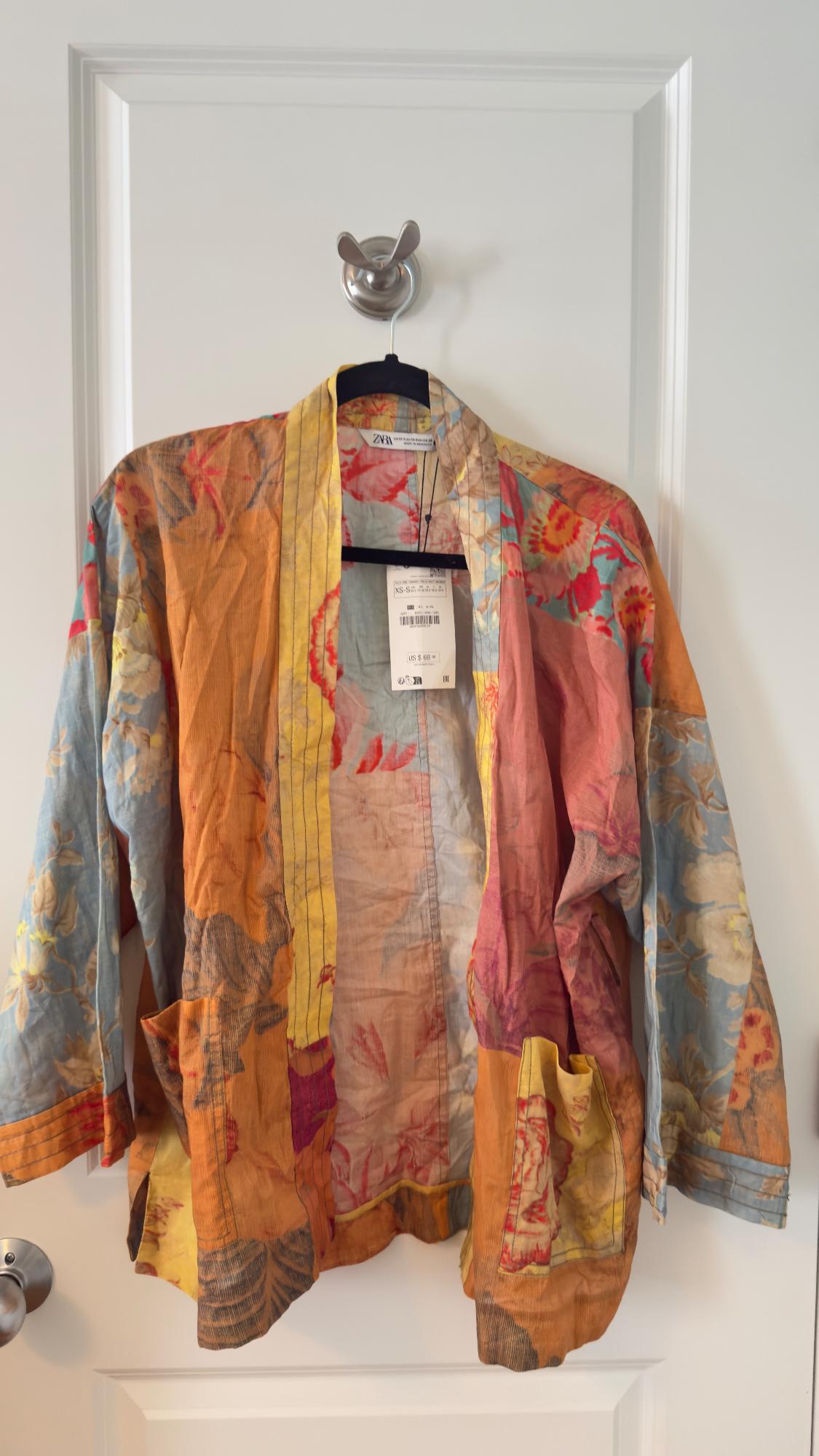 Colorful jacket with floral print hanging on a white door. Visible tag with price of $69.90.