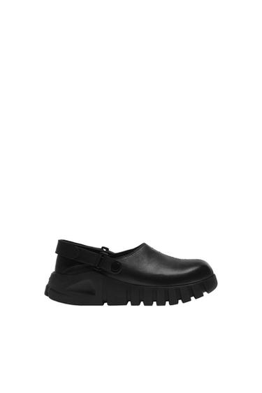 Black clog-style shoe with a thick, chunky sole and back strap, on a white background.