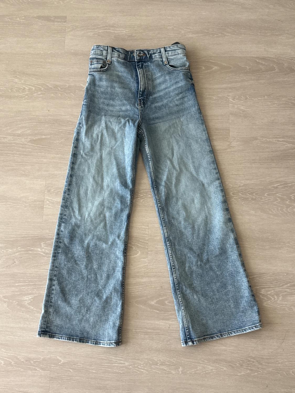 Light blue high-rise wide-leg jeans laid out on a light wood floor. Casual and relaxed style.