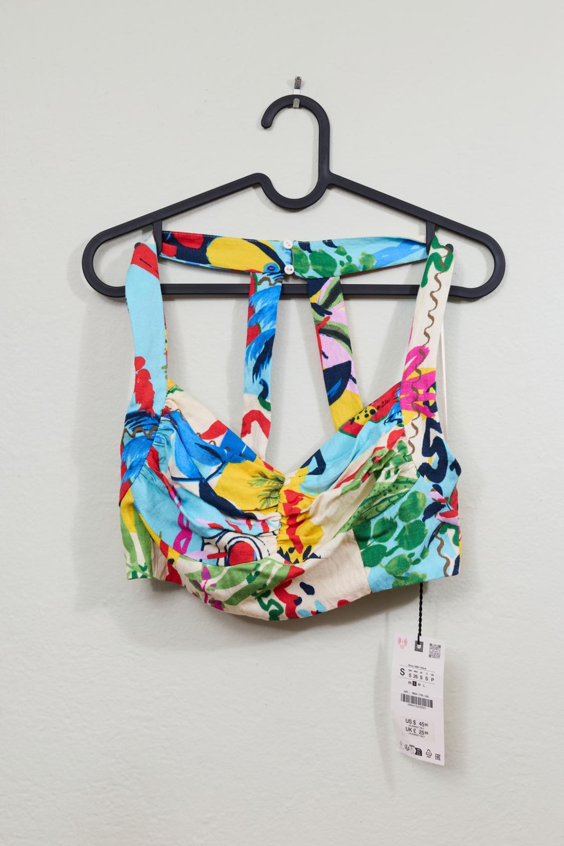 Short top with a colorful print and spaghetti straps, hanging on a hanger. Label with text: S 26 S S P, XS S M L, US $ 45.90, UK £ 25.99.