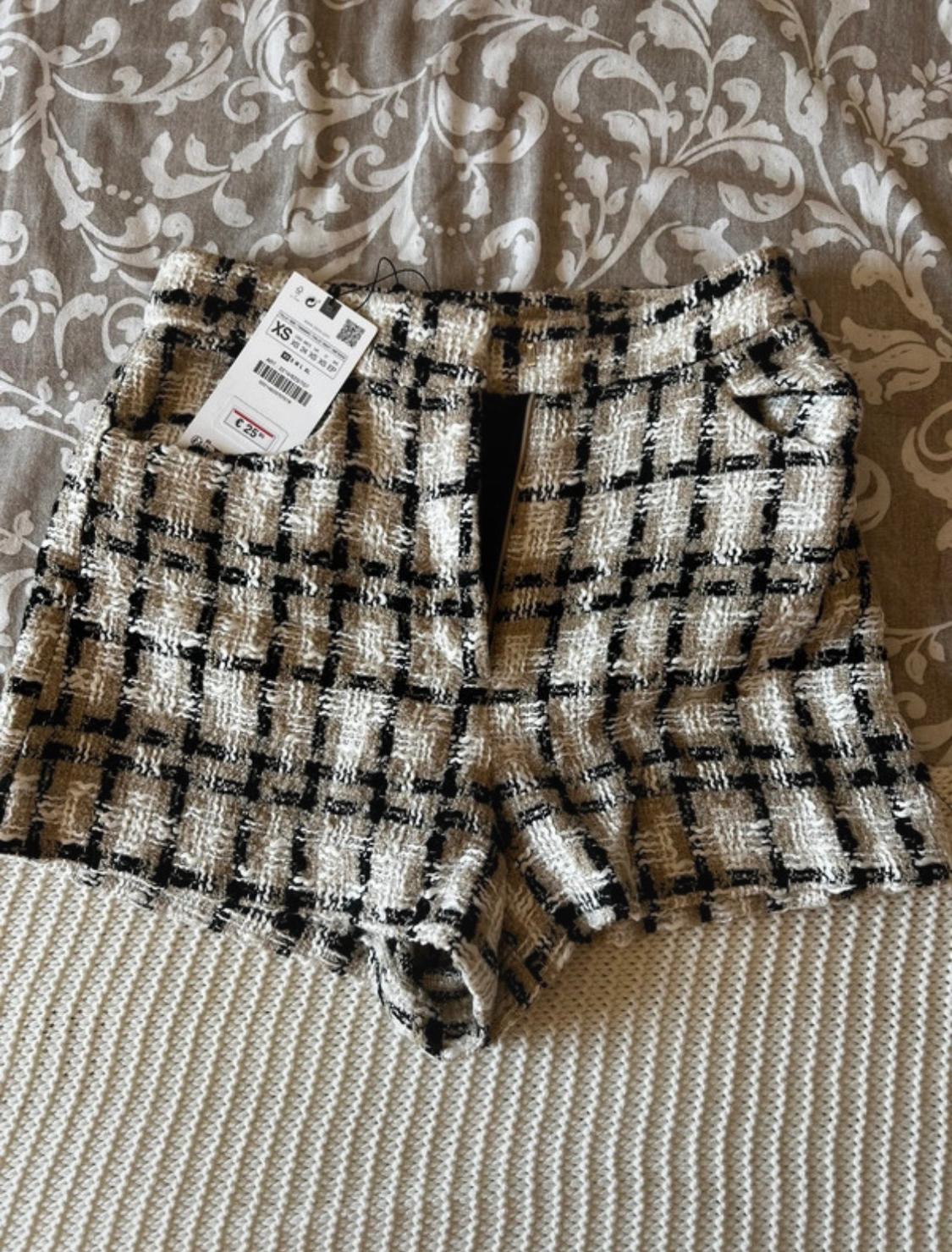 Black and white checked fabric shorts on a bed with a patterned bedspread. Visible tag with price of €25.