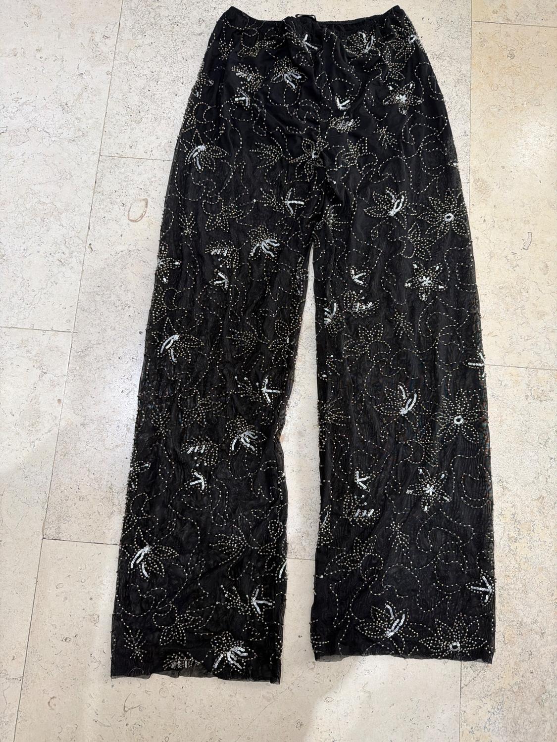 Wide-leg semi-sheer black trousers with silver sequin floral embroidery, on a light-tiled floor.