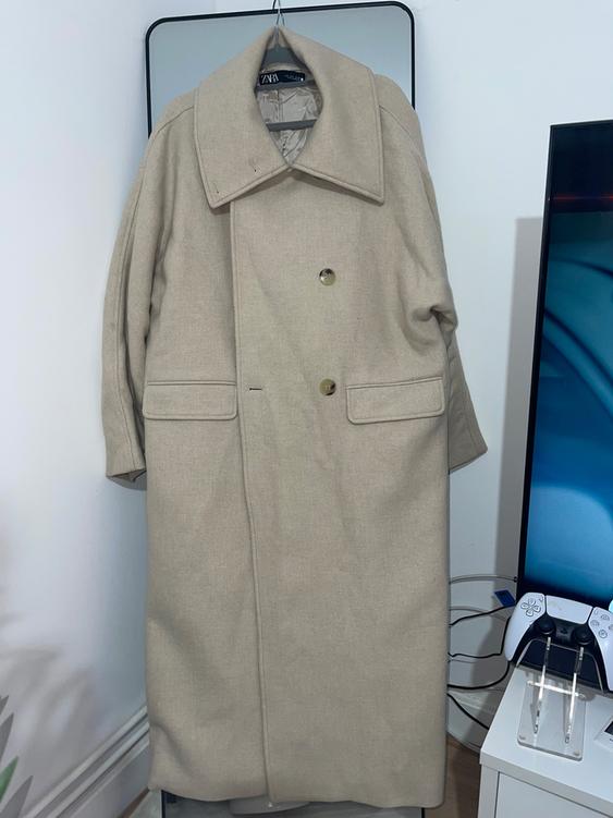 Beige coat hanging on a mirror, with two visible buttons. To the right, a video game controller on a white table.