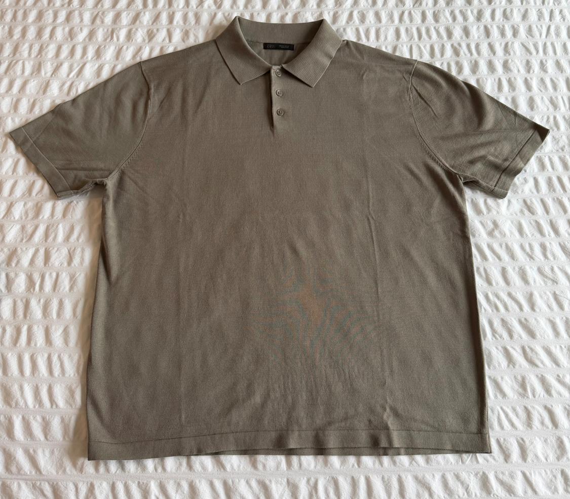 Olive green short-sleeve polo shirt with a classic collar and three buttons, laid out on a textured white surface.