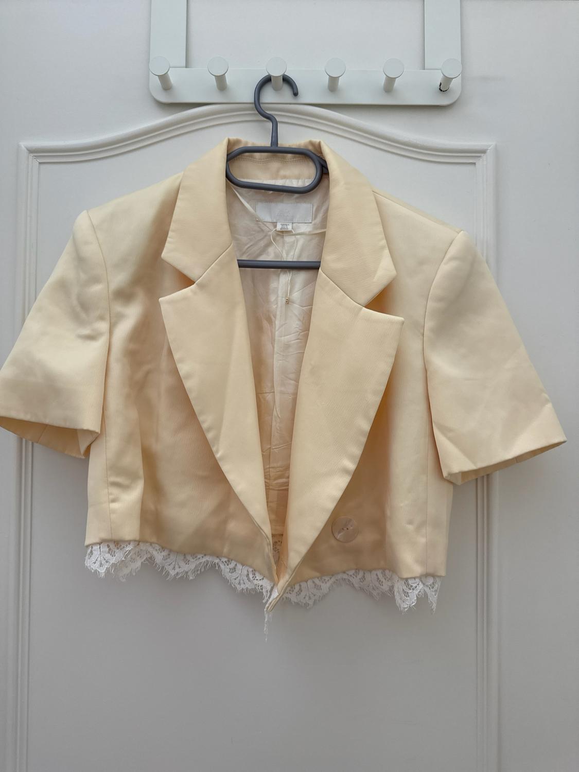 Short yellow short-sleeved jacket with a white lace hem, hanging on a hanger over a white door.