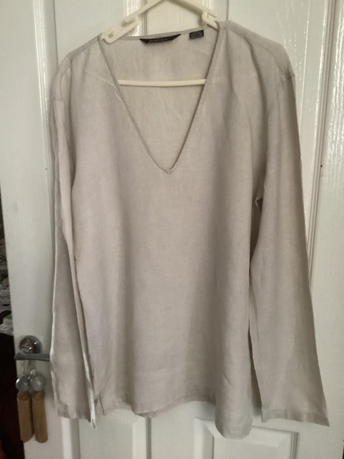 Lightweight beige long-sleeved shirt with a deep V-neck, hanging from a hanger on a white door with a silver knob and tassels.