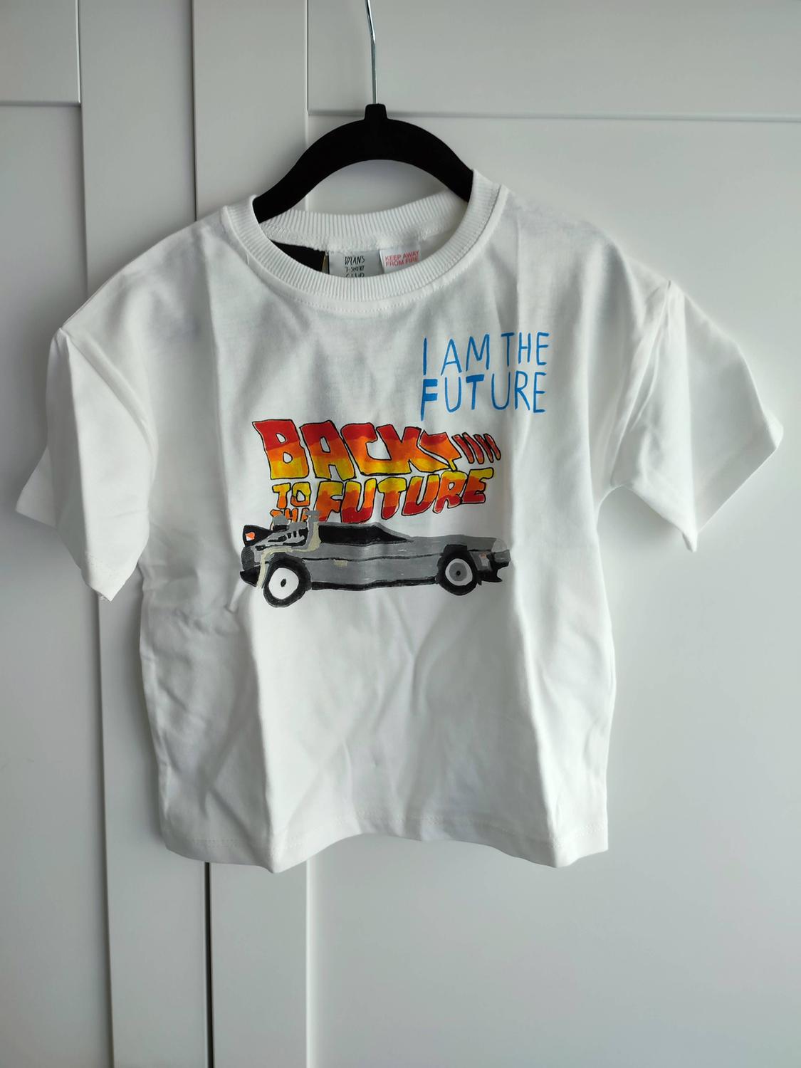 White T-shirt on a hanger with a car and text "I AM THE FUTURE", "BACK TO THE FUTURE", "DYLAN'S T-SHIRT CLUB", "KEEP AWAY FROM FIRE".