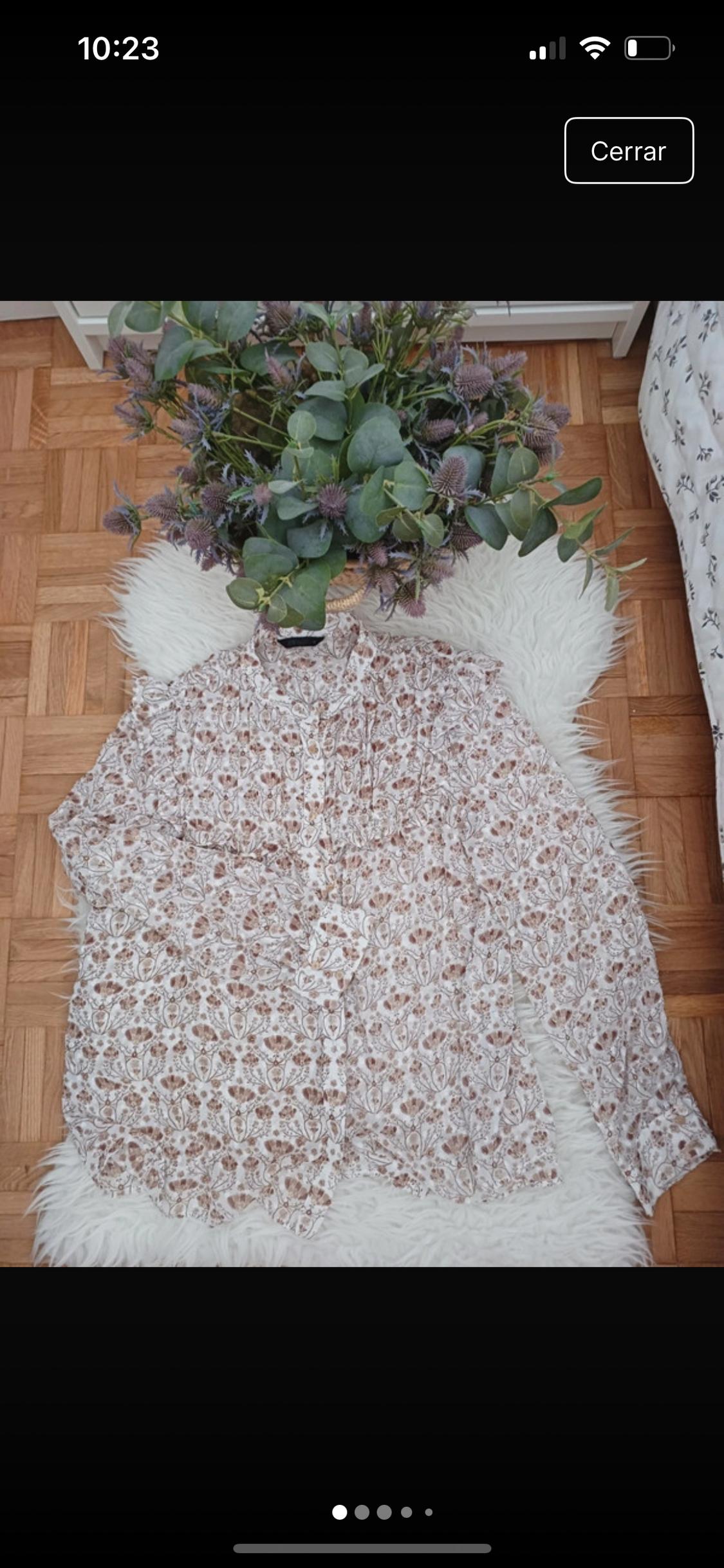 Μπλούζα με floral σχέδιο σε καφέ αποχρώσεις πάνω σε λευκό χαλί, με ένα μπουκέτο πράσινα και μωβ λουλούδια από πάνω. Φόντο παρκέ.