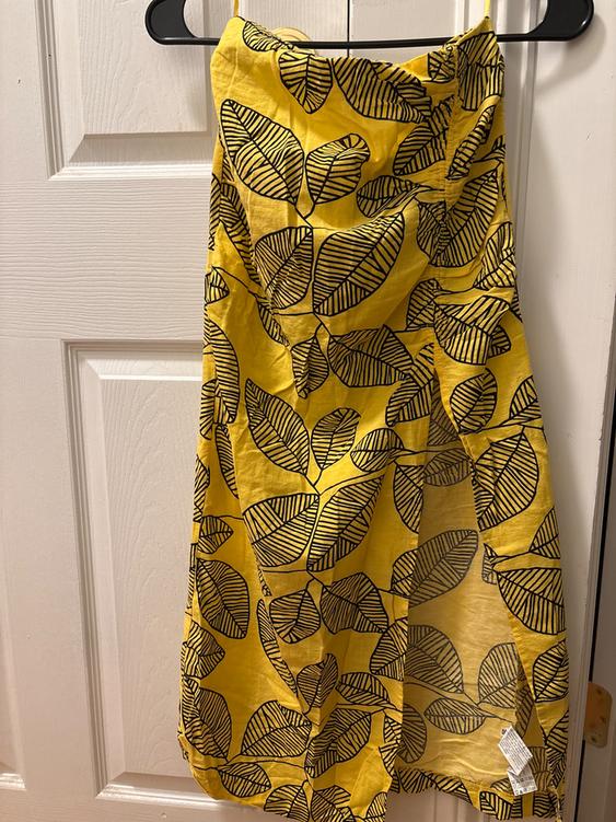 Yellow dress with black leaf print hanging on a hanger in front of a white door.