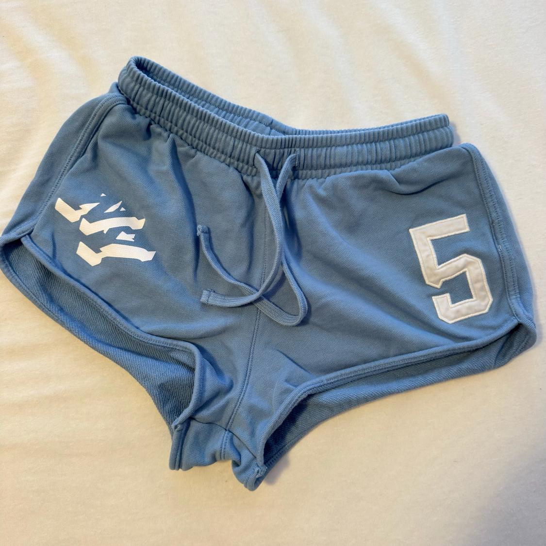 Light blue sports shorts over white fabric. They have an elasticated waistband with a drawstring, a white graphic and the number 5.