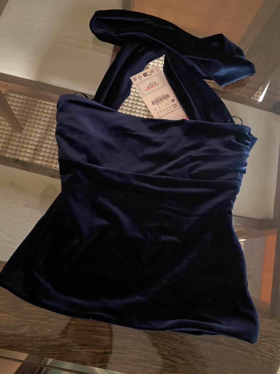 Dark blue velvet top on a glass table. Visible tag with a price of 25 and size XS. Warm and elegant atmosphere.