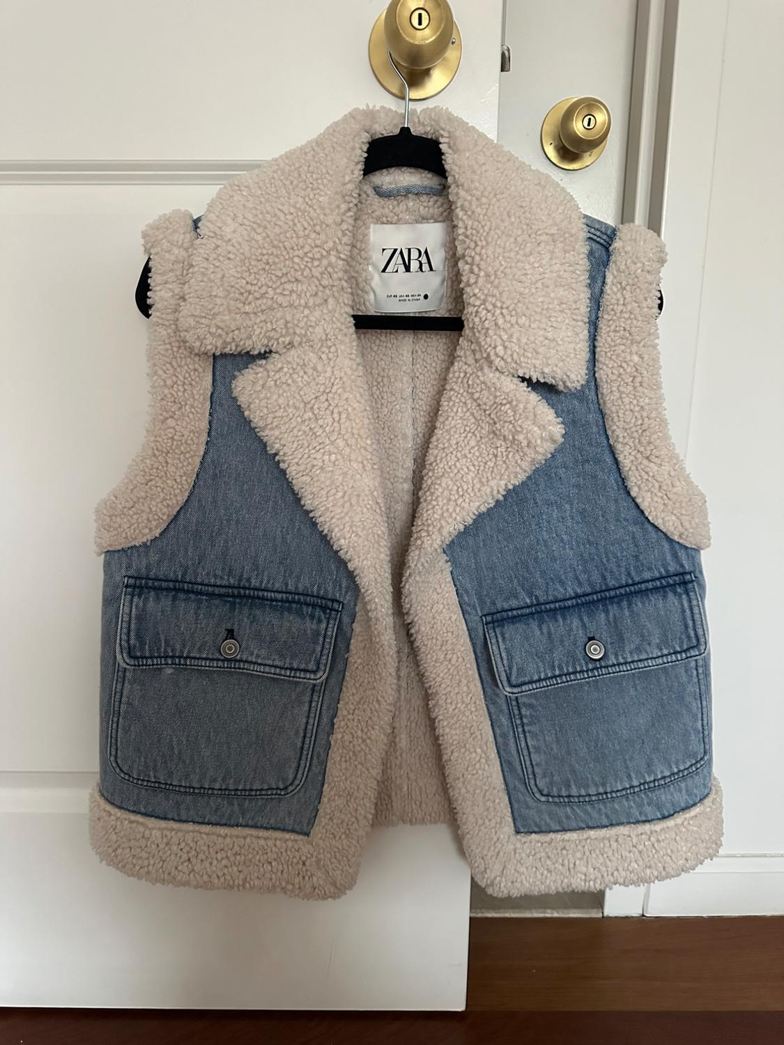 Denim vest with sherpa lining hanging on a white door. Visible tag with the text "ZARA".