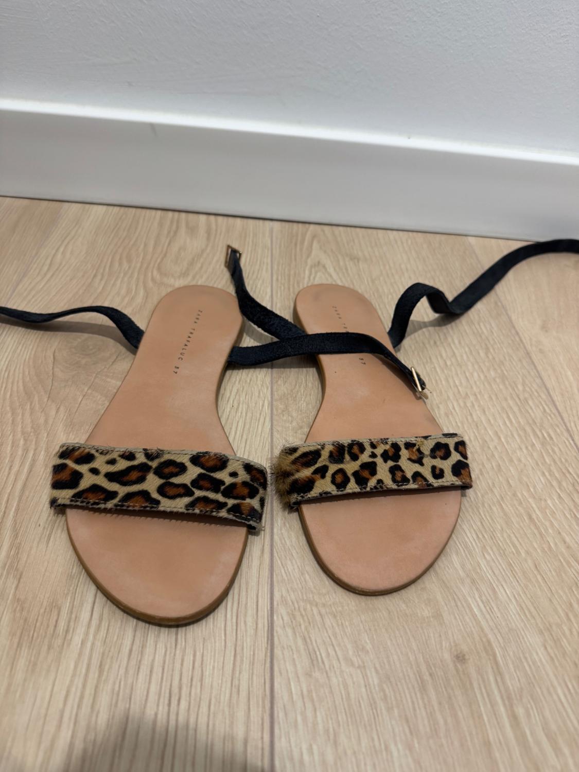 Flat sandals on a wooden floor with a leopard-print strap and black ribbons. Text on the insole: ZARA TRAFALUC 37.