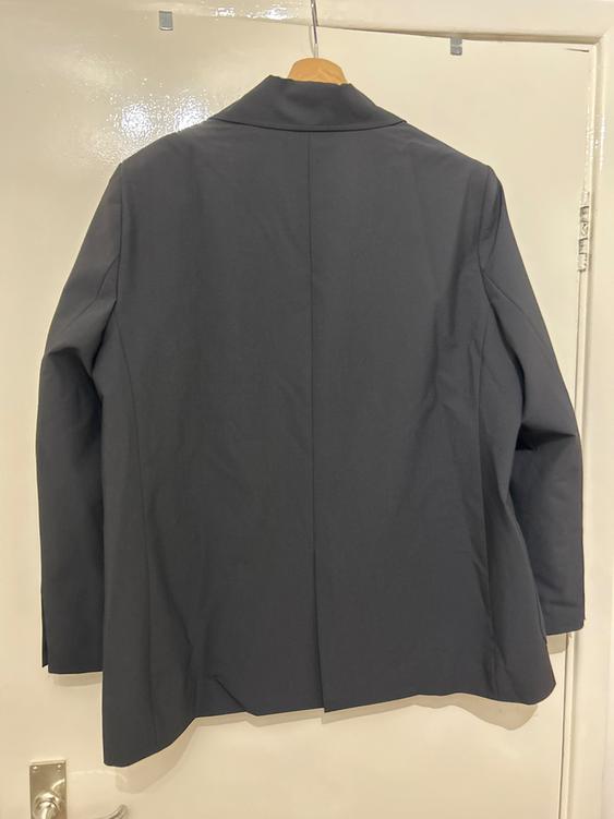 Grey jacket hanging on a wooden hanger over a white door. The jacket is viewed from behind, showing its simple design.
