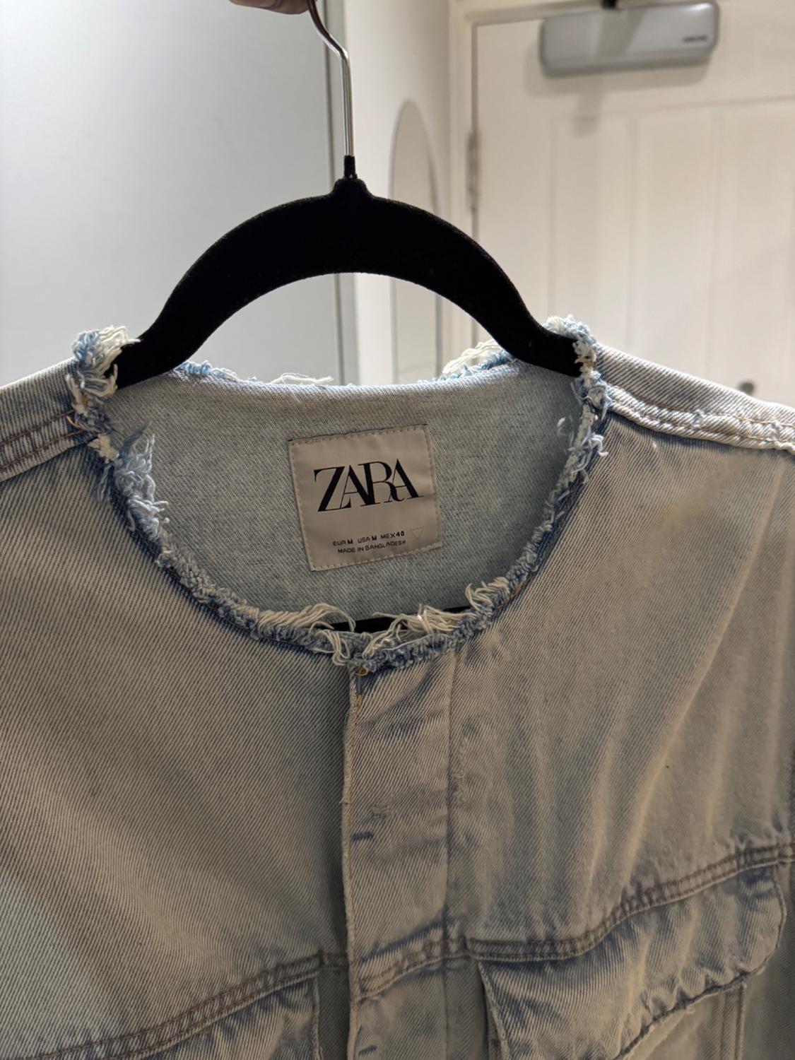 Light blue denim shirt with frayed collar on a black hanger. Visible label: "ZARA". White indoor background.