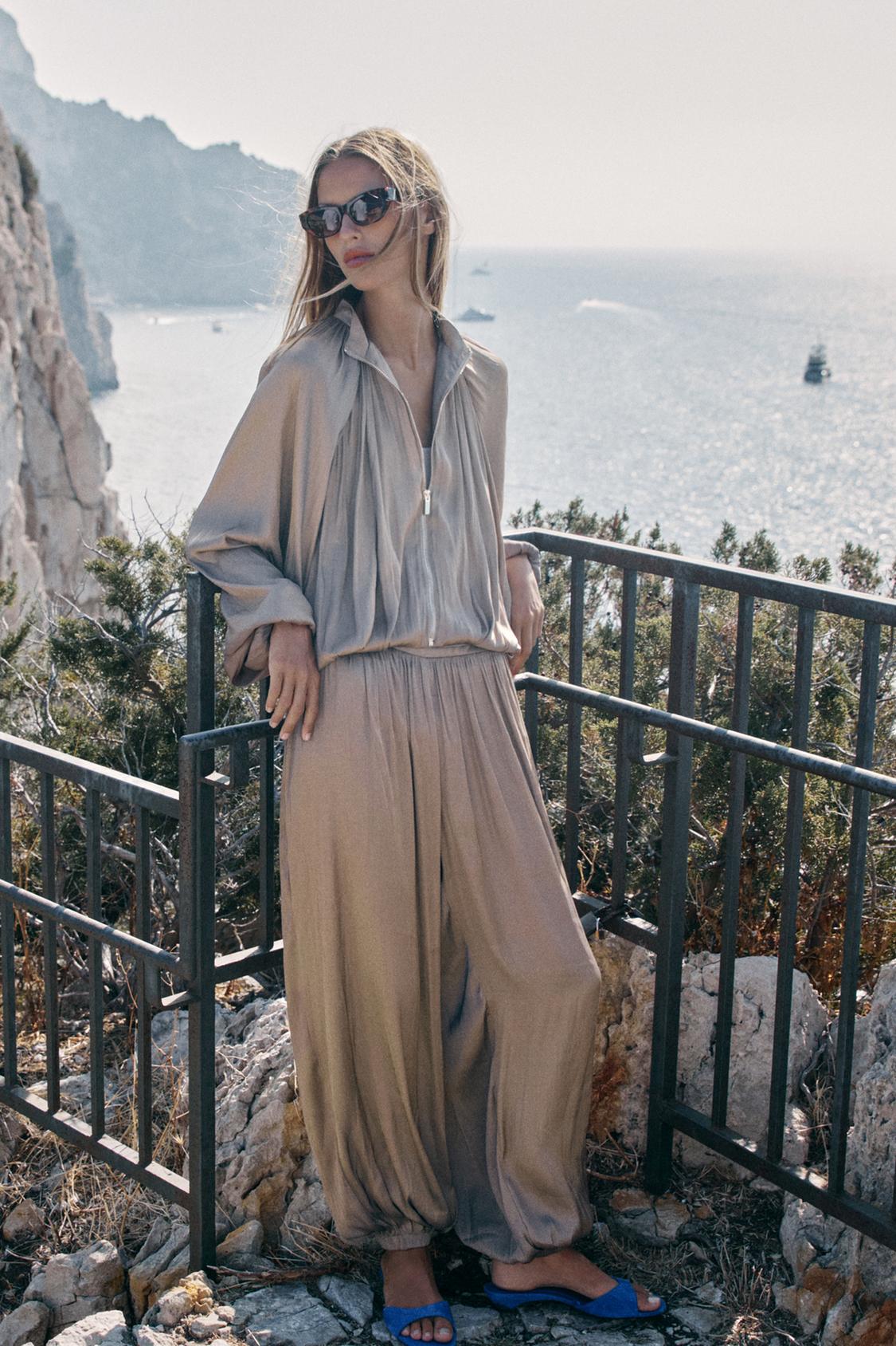 Conjunto de chaqueta fluida beige con cremallera, mangas largas y pantalón ancho a juego con bajo fruncido.