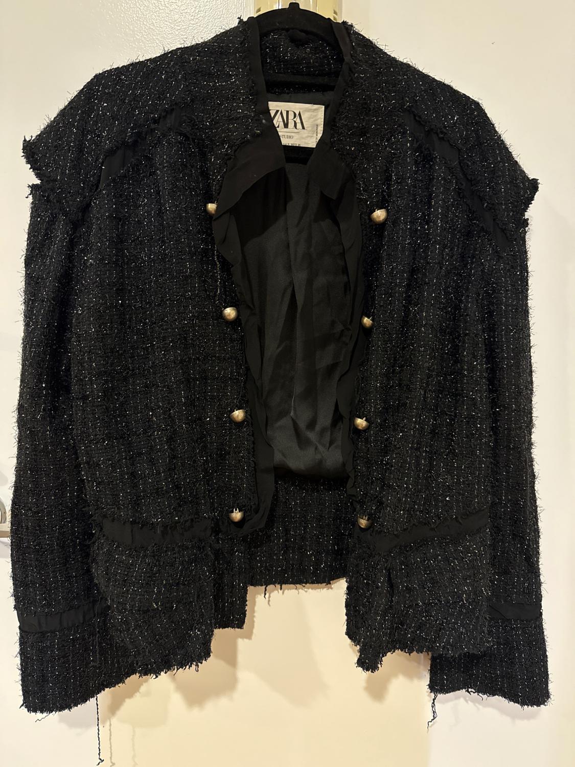 Textured black jacket with gold buttons, hanging on a hanger. Visible label with the brand "ZARA". White background.