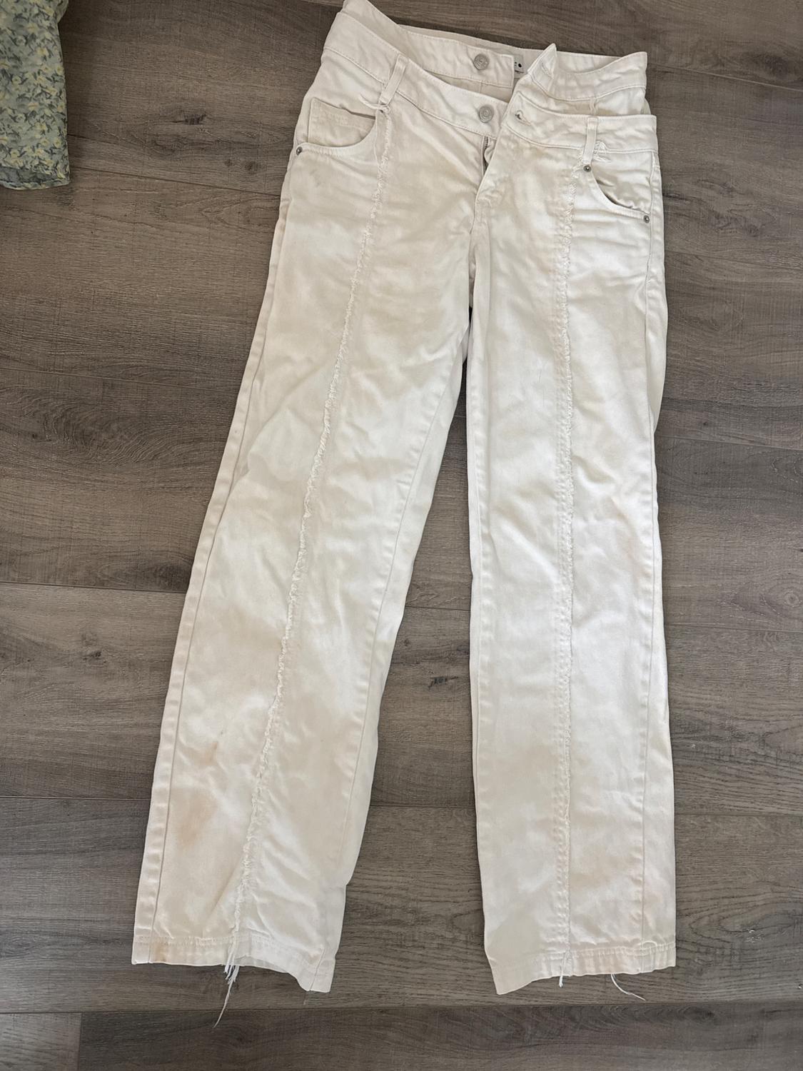 White denim pants with frayed front seams, laid out on a wooden floor.
