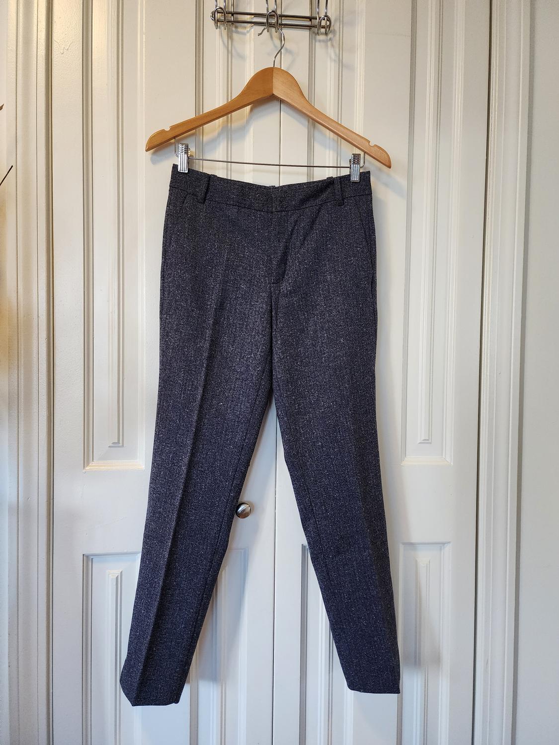 Gray pants hanging on a wooden hanger in front of a white paneled door.