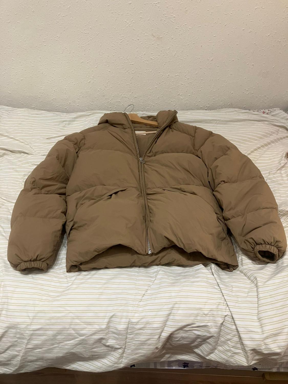 Brown padded jacket with zip, placed on a bed with white pinstripe sheets.