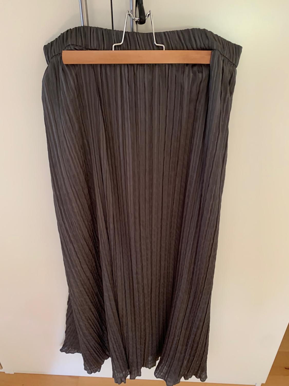 Dark grey pleated maxi skirt hanging on a wooden hanger over a white door.