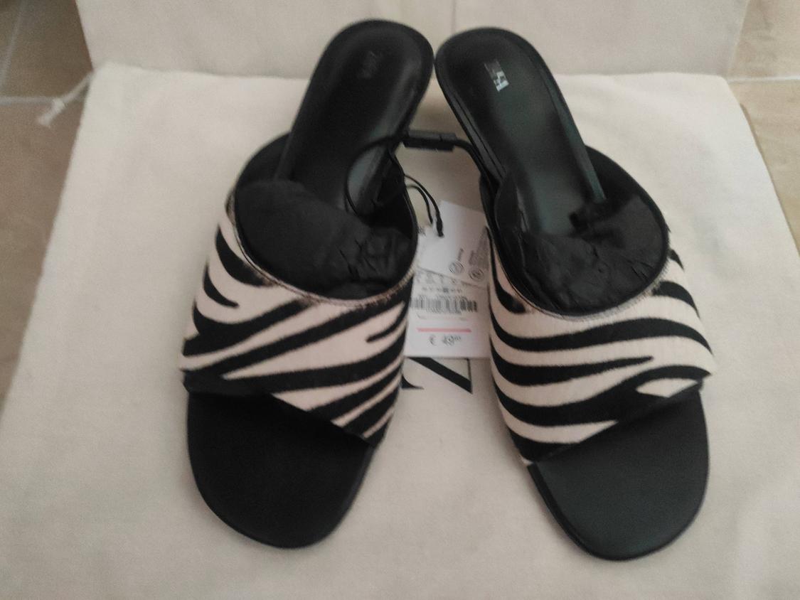 Black and white zebra print low-heeled sandals on a light surface. Visible tags between the sandals.