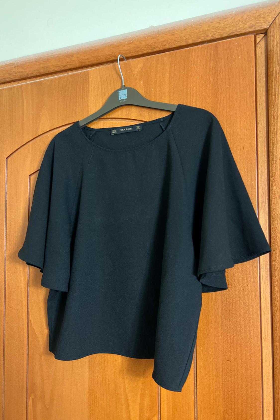 Front view of a loose, short-sleeved black blouse hanging on a hanger.