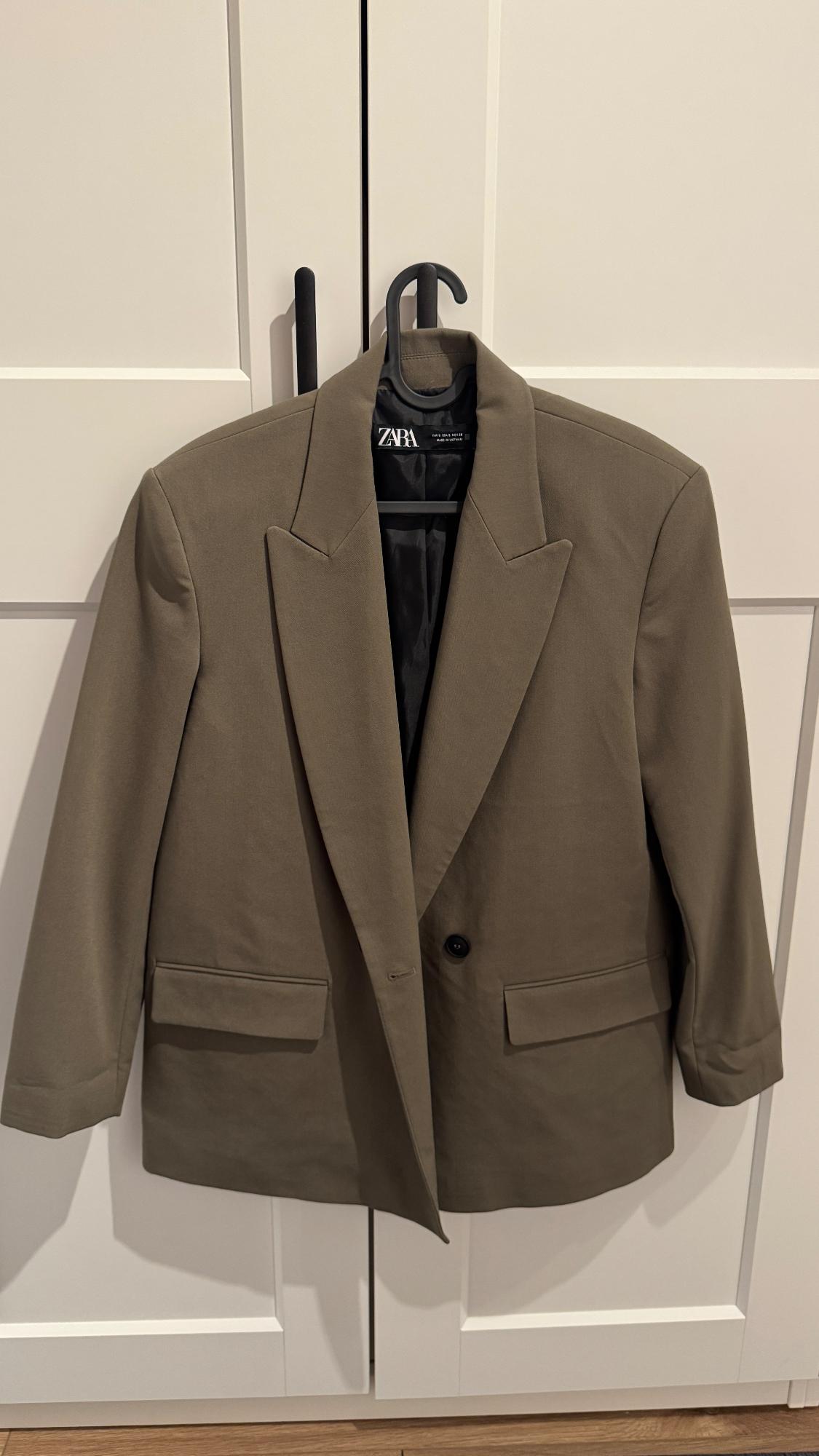 Brown Zara jacket hanging on a black hanger in front of a white wardrobe.