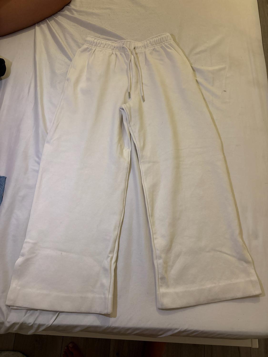 White wide-leg sports trousers with an elasticated waistband and drawstring, laid out on a white sheet.