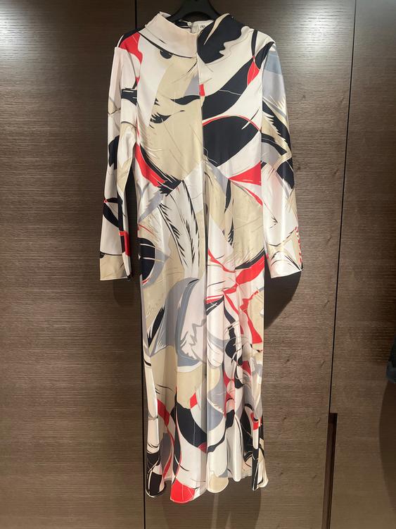 Long dress with an abstract print in beige, black, red, and white tones, hanging on a hanger against a dark wooden background.