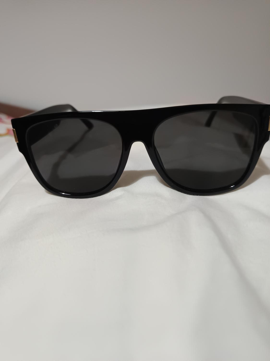 Black sunglasses with thick frames on a white surface, light grey background.