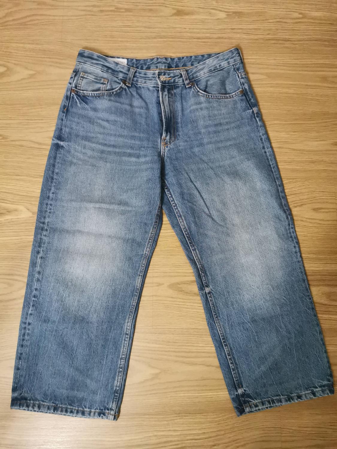 Blue wide-leg distressed jeans laid out on a light wood floor. Casual flat lay composition.