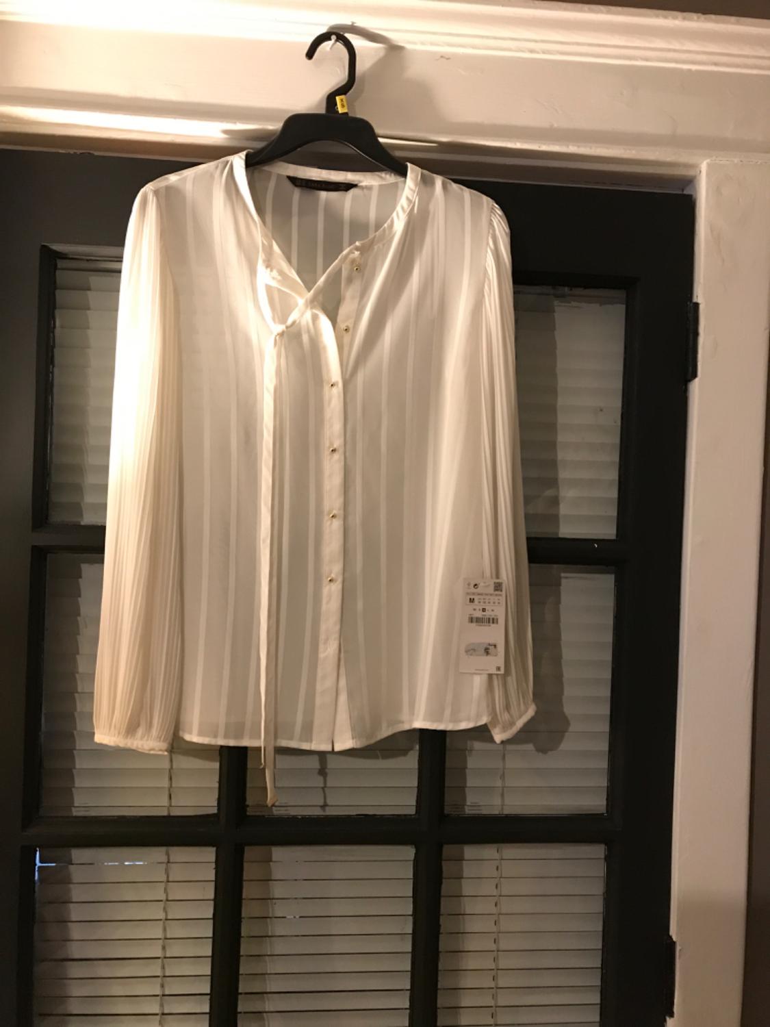 Front view of a white blouse with vertical stripes, gold buttons and a tie at the neck.