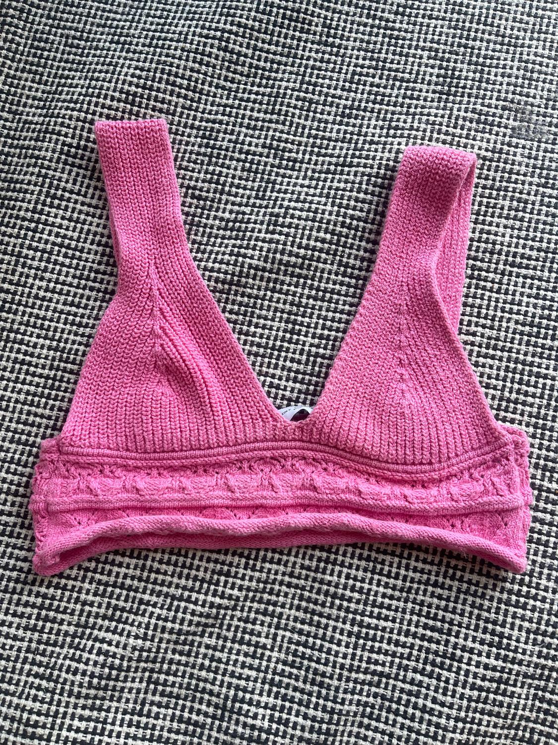 Pink knitted bra on a black and white fabric background with a small checked pattern.