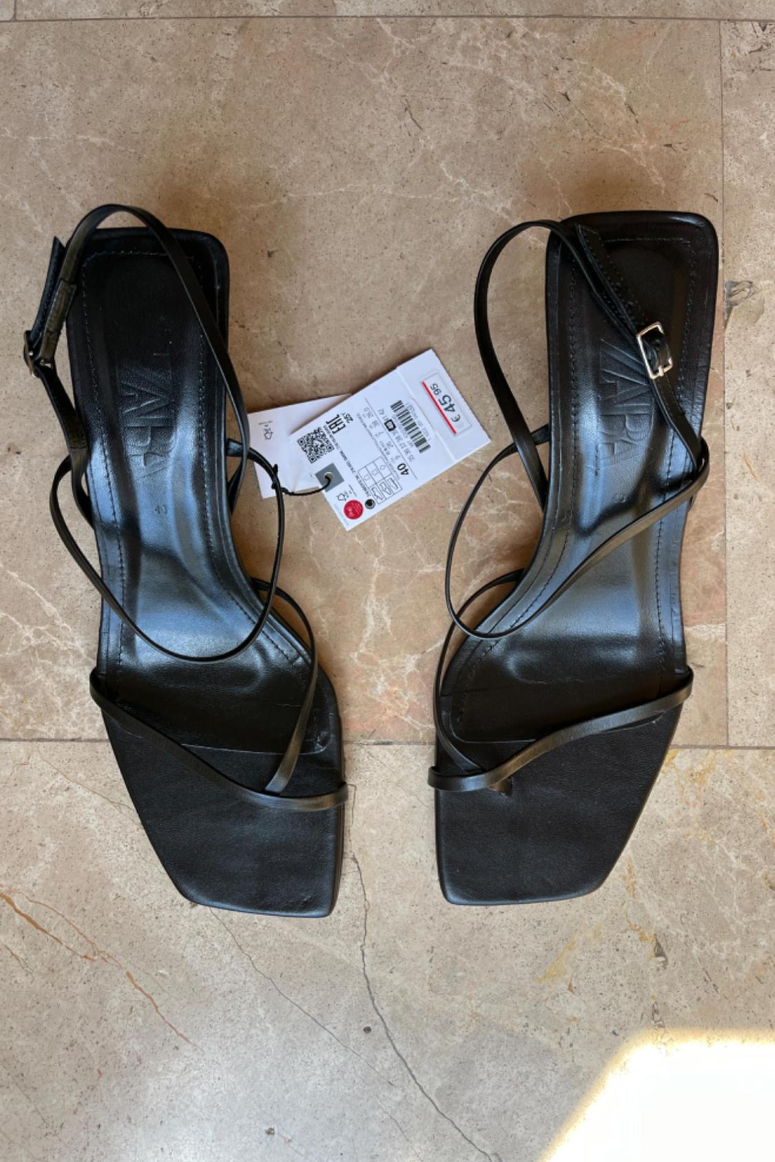 Front view of black strappy sandals with a square sole and visible label.