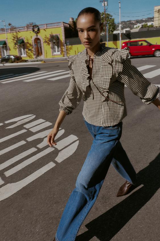 Sada kárované halenky s volány a mašlí u krku, dlouhými nabíranými rukávy a rovnými modrými džíny.