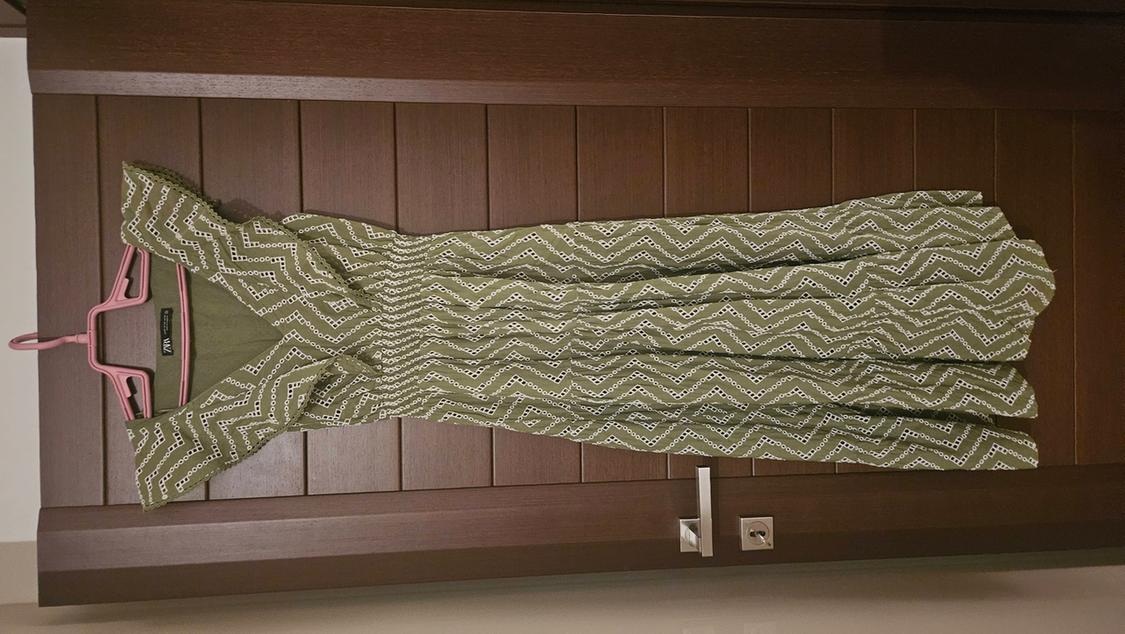 Green dress with white zigzag print hanging on a pink hanger over a wooden door. Visible tag: "Rangriti".