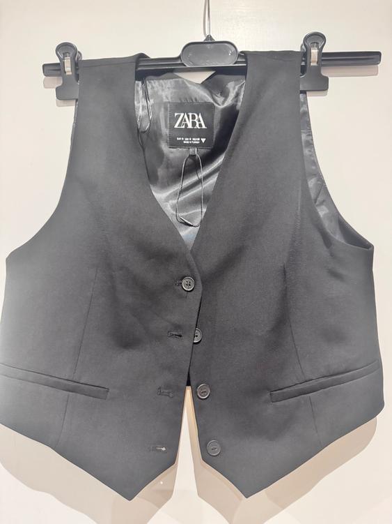 Black formal waistcoat hanging on a hanger, with a visible Zara label inside. White background.