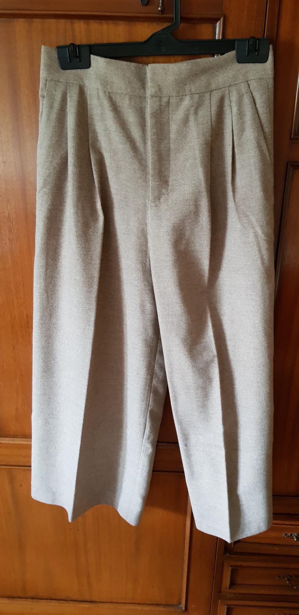 Beige trousers hanging on a black hanger against a wooden background. Classic design with pleats at the top.