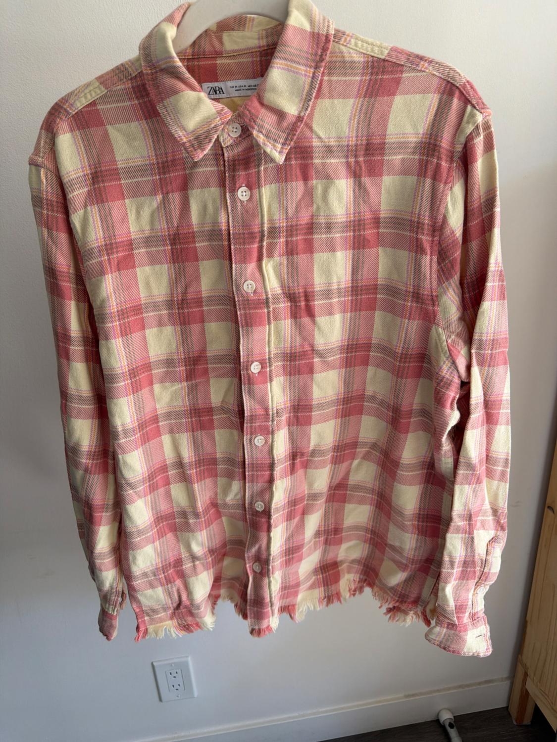 Red and beige checked shirt hanging on a hanger, with white buttons and frayed edges, on a white background.