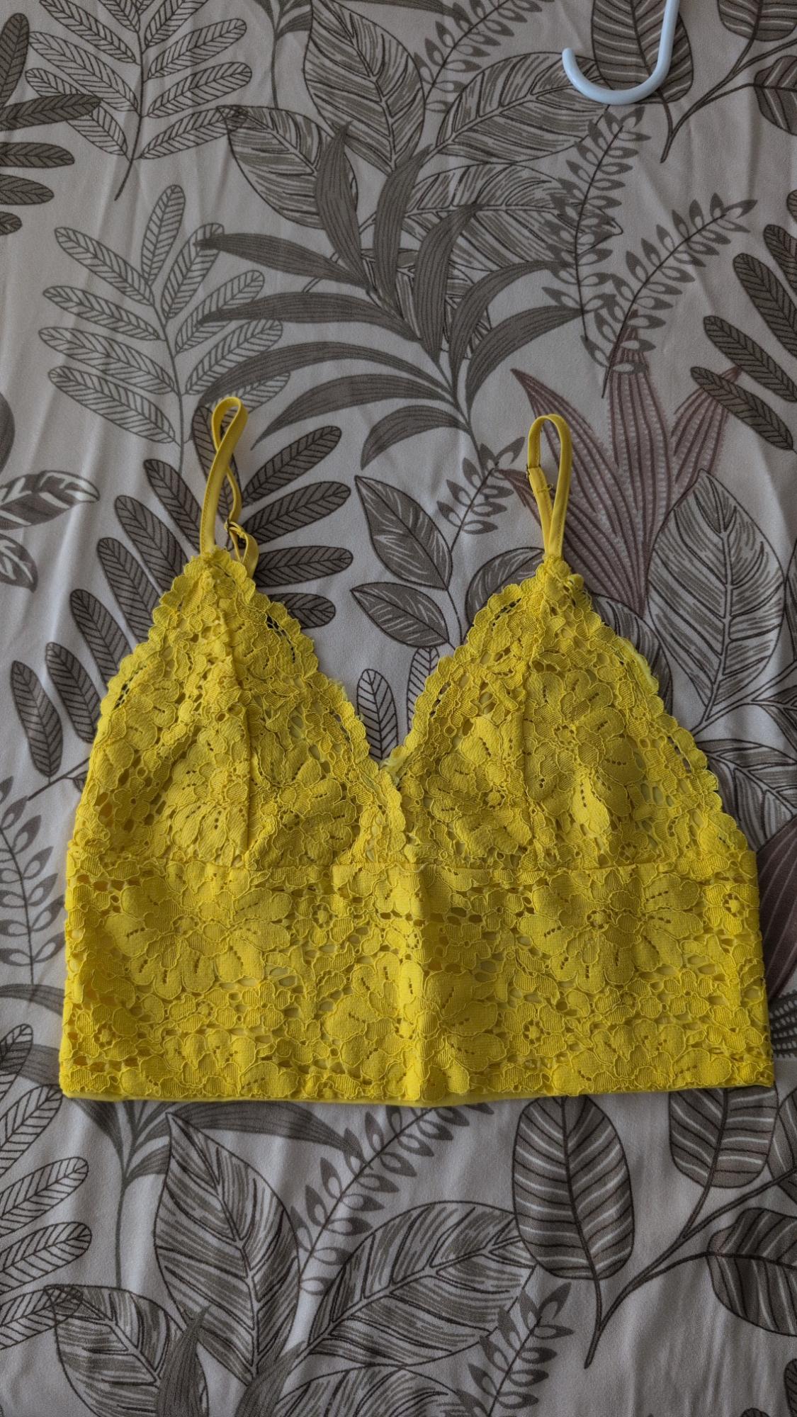 Yellow floral lace camisole with thin straps, photographed on a botanical leaf-print sheet.