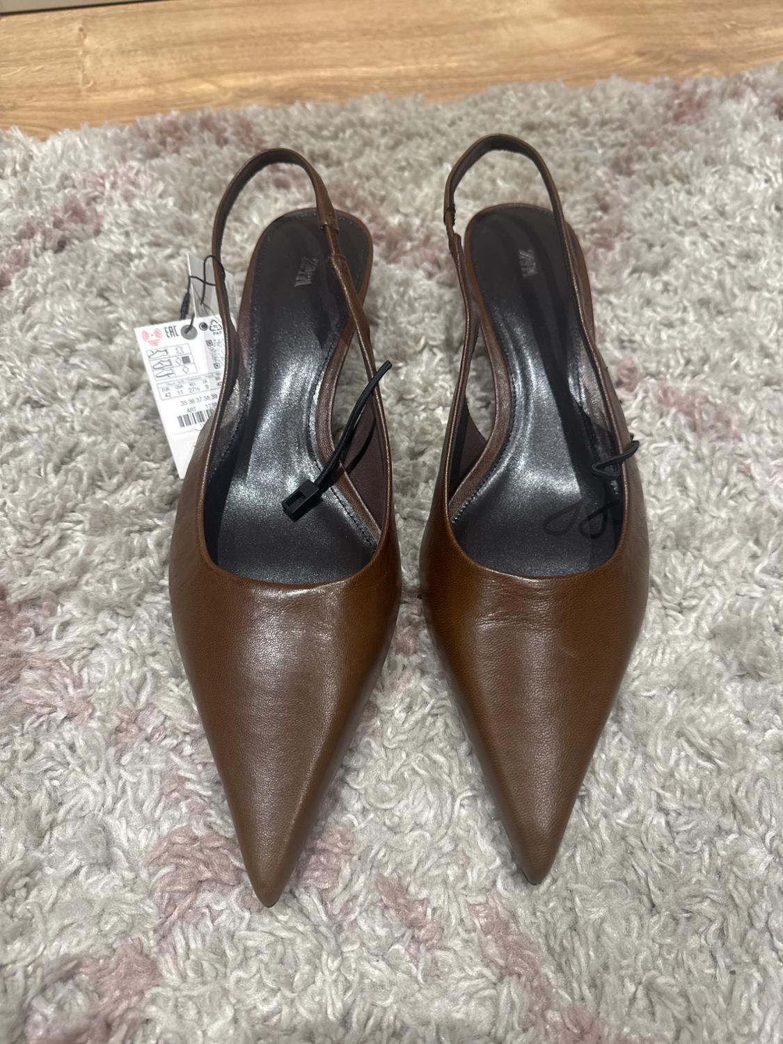 Brown, pointed-toe slingback shoes on a grey carpet. Visible tag on the left shoe.