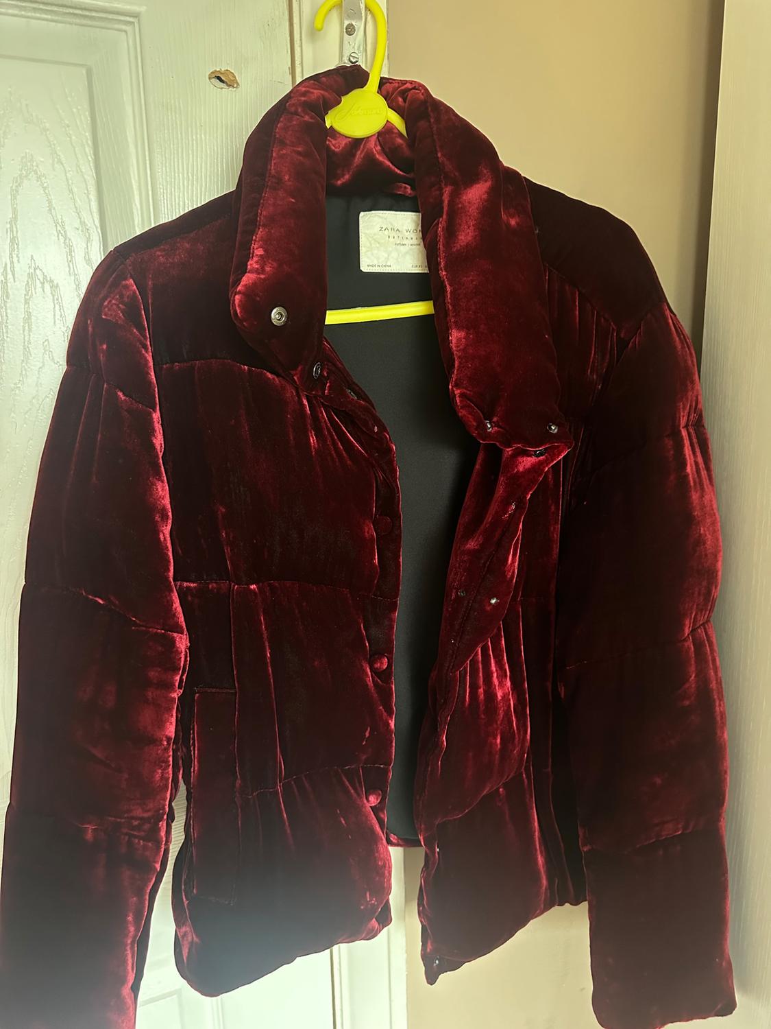 Dark red velvet quilted jacket hanging on a yellow hanger over a white door.